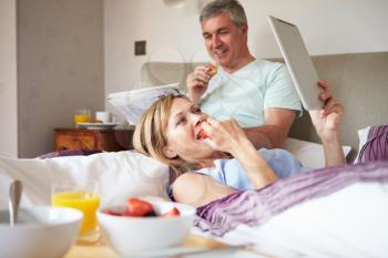Couple Eating Breakfast In Bed With Paper And Digital Tablet