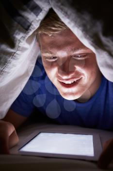 Teenage Boy Using Digital Tablet In Bed At Night
