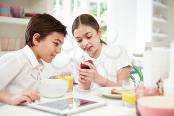Schoolchildren With Digital Tablet And Mobile At Breakfast