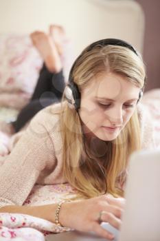 Teenage Girl Lying On Bed Using Laptop Wearing Headphones