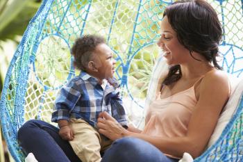 Mother With Baby Son Relaxing On Outdoor Garden Swing Seat