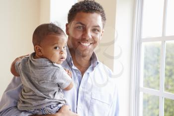 Smiling Father Standing By Window With Baby Son At Home