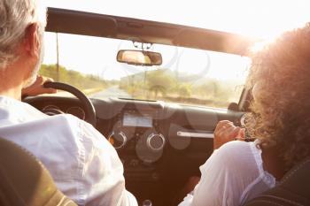 Mature Couple Driving Along Country Road In Open Top Car