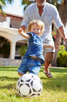 Grandfather Playing Football With Grandson In Garden
