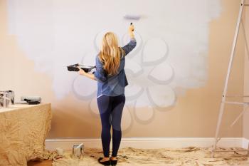 Woman Decorating Room Using Paint Roller On Wall