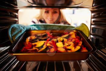 Woman Putting Dish Of Vegetables Into Oven To Roast