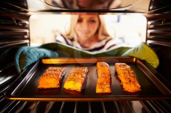 Woman Putting Salmon Fillets Into Oven To Cook