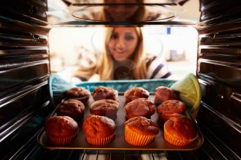 Woman Taking Tray Of Baked Muffins Out Of The Oven