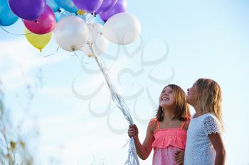 Two Young Girls Holding Bunch Of Colorful Balloons Outdoors