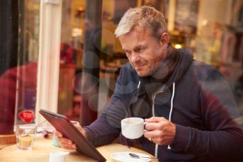 Man Viewed Through Window Of Caf Using Digital Tablet