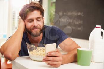 Young Man Eating Breakfast Whilst Using Mobile Phone