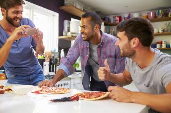 Three Male Friends Making Pizza In Kitchen Together