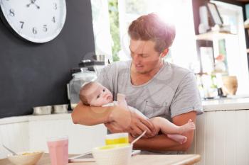 Father Holding Newborn Baby Daughter At Kitchen Table