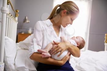 Mother Dressed For Work Holding Baby In Bedroom