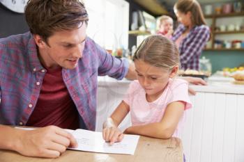 Father Reading Book With Daughter At Kitchen Table