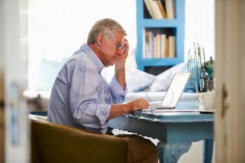 Senior Man At Desk Working In Home Office With Laptop