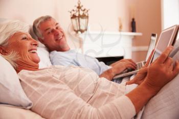 Senior Couple Lying In Bed Using Digital Devices