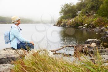 Senior woman with a hat sitting by the lake, admiring the view