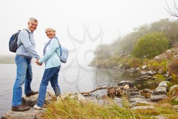 Senior couple standing by a lake, smiling to a camera