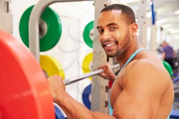 Smiling man holding barbells on a rack at a gym
