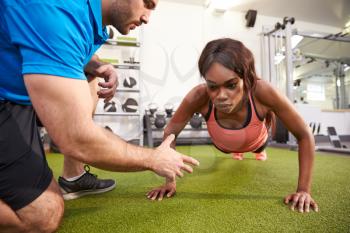Young woman doing push ups under supervision of a trainer