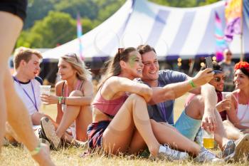 Friends sitting on the grass taking selfie at music festival