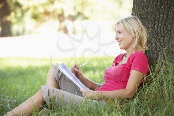 Middle Aged Woman Sketching In Countryside Leaning Against Tree
