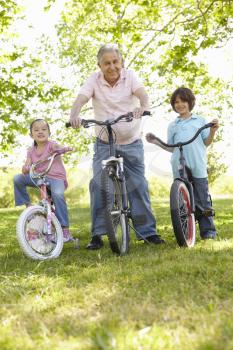 Hispanic Grandfather With Grandchildren In Park Riding Bikes