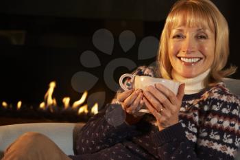 Mature woman relaxing in front of fire at home