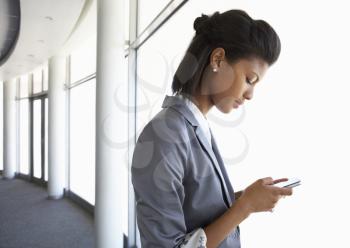 Young Businesswoman Standing In Corridor Of Modern Office Building Using Mobile Phone