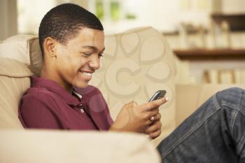 Teenage Boy Sitting On Sofa At Home Texting On Mobile Phone
