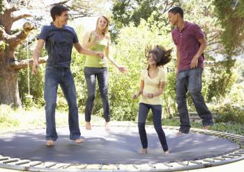 Four Teenage Friends Jumping On Trampoline In Garden