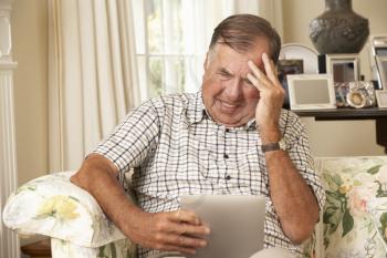 Frustrated Retired Senior Man Sitting On Sofa At Home Using Digital Tablet