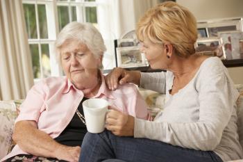 Adult Daughter Visiting Unhappy Senior Mother Sitting On Sofa At Home