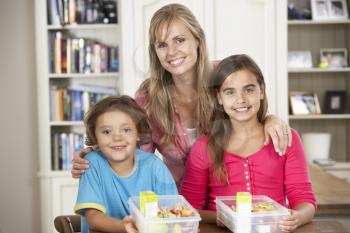 Mother Giving Two Children Healthy Lunchboxes In Kitchen