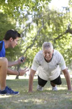 Senior Man Working With Personal Trainer In Park