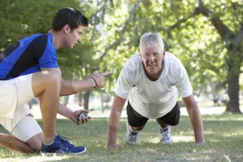 Senior Man Working With Personal Trainer In Park
