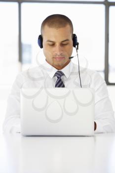 Businessman Sitting At Desk In Office Using Laptop Wearing Headset