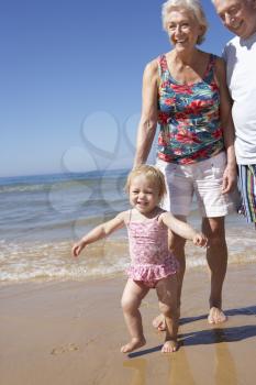 Grandparents And Granddaughter Walking Along Beach