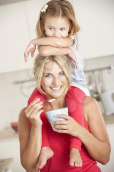 Daughter Sitting On Shoulders Whilst Mother Eats Yoghurt