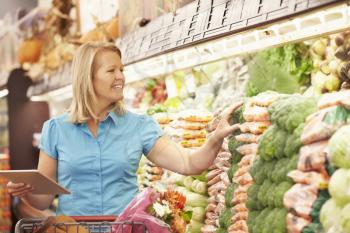 Woman Reading Shopping List From Digital Tablet In Supermarket