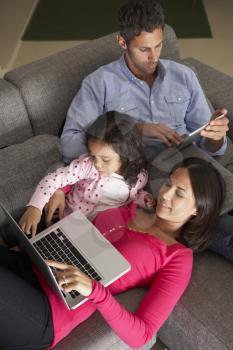 Hispanic Family On Sofa Using Laptop And Digital Tablet