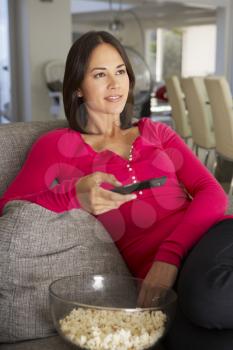 Hispanic Woman On Sofa Watching TV Eating Popcron