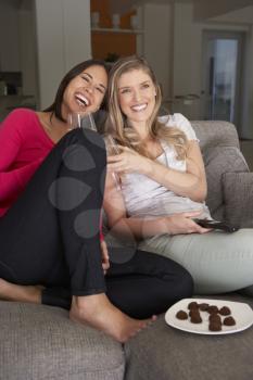 Two Women Sitting On Sofa Watching TV Drinking Wine