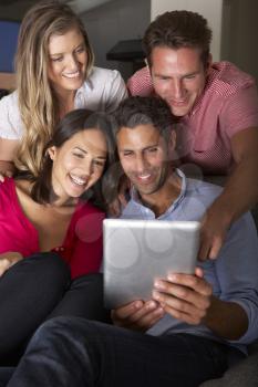Group Of Friends Sitting On Sofa Looking At Digital Tablet