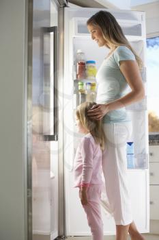 Mother And Daughter Choosing Snack From Fridge