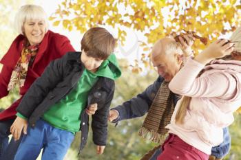 Grandparents And Grandchildren With Leaves In Autumn Garden
