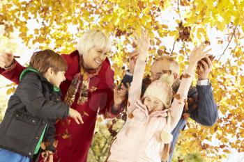 Grandparents And Grandchildren With Leaves In Autumn Garden