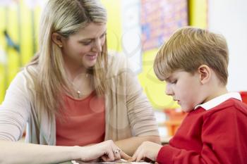 Teacher Helping Male Pupil With Reading At Desk