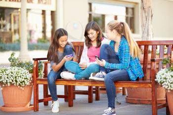 Group Of Girls Sitting In Mall Using Mobile Phones